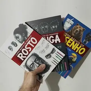 Três livros do Curso Básico de Desenho segurados em uma mão